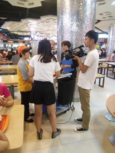 电视台记者在美食广场现场经理陪同下采访王秀荣大姐